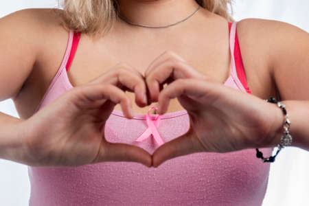 Caucasian girl making a heart with her hands over a breast cancer ribbon.