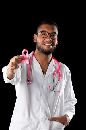 dark skin doctor with pink stethoscope and pink awareness breast cancer ribbon, on a black background.の写真素材