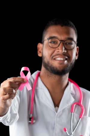 dark skin doctor with pink stethoscope and pink awareness breast cancer ribbon, on a black background.の写真素材
