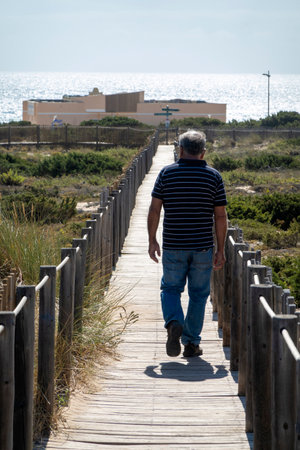 Man walking through the beautiful view of the Guincho wooden pathway through the sand dunes, located in Sintra, Portugal.の写真素材