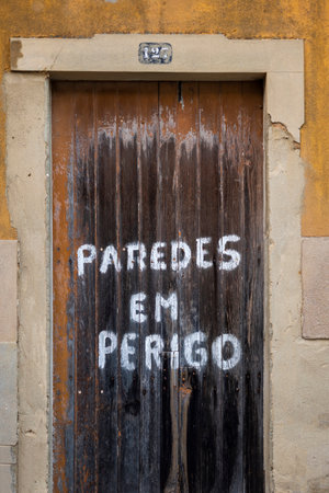old wooden door with lettering "walls in danger" in Fuseta village, Portugal.の写真素材
