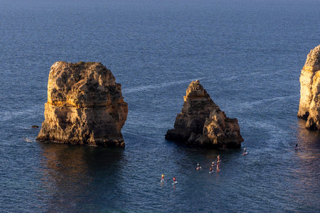 Paddleboarding or stand up paddle sport in the coastline of Lagos, Algarve, Portugal at sunrise.