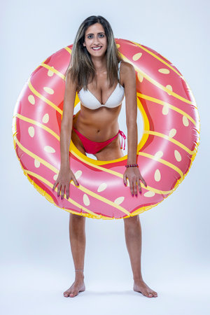 Woman in bikini with large inflatable swimming ring over a gray background.の写真素材