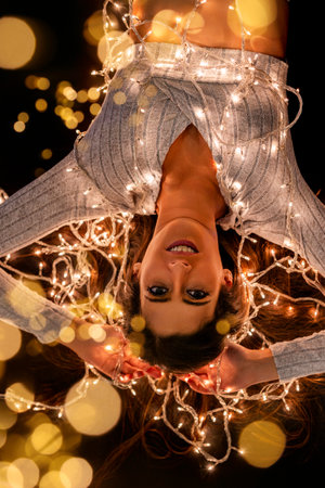 Young woman holding Christmas's string lights over a black background in different poses.の写真素材