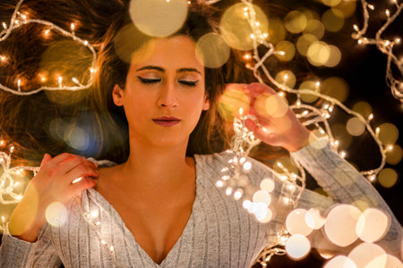 Young woman holding Christmas's string lights over a black background in different poses.の写真素材