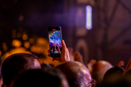 Close view of a fan using a modern cellphone to record a live concert.
