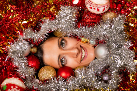 Young woman face closeup surrounded by Christmas's red, silver and golden balls.の写真素材