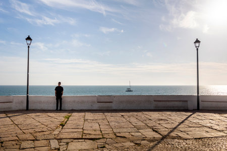 Close view of a lonely man watching the ocean with two street lights on the side.の写真素材
