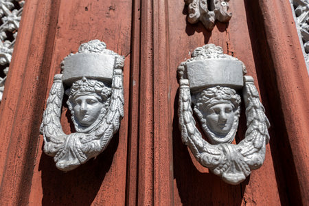 Close up view of two Old decorated door knockers in a wooden red door.