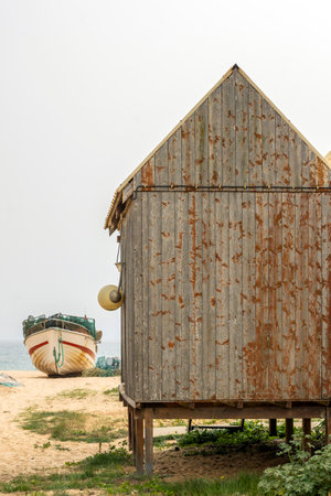 Traditional Portuguese fishing boat and small storage house anchored on the beach in the Algarve region.の写真素材