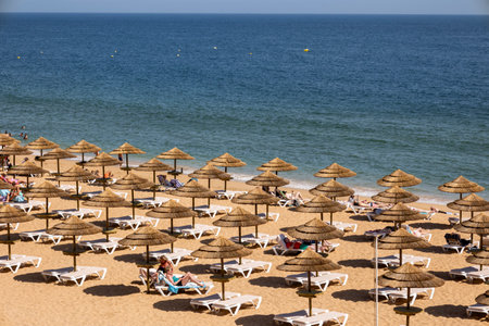 ALBUFEIRA, PORTUGAL - 7th MAY 2024: Thatched roof parasols and lounge chairs in a beach of Albufeira, Portugal.のeditorial素材