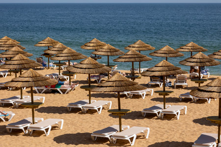 Thatched roof parasols and lounge chairs in a beach of Albufeira, Portugal.の写真素材