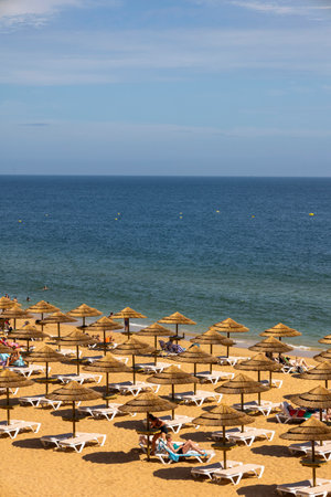 ALBUFEIRA, PORTUGAL - 7th MAY 2024: Thatched roof parasols and lounge chairs in a beach of Albufeira, Portugal.のeditorial素材
