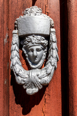 Close up view of an old decorated door knockers in a wooden red door.の写真素材