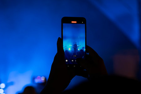 Person holding smartphone records live concert during music and light show.のeditorial素材