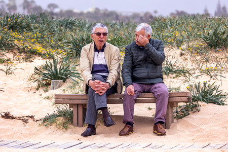 ARMACAO DE PERA, PORTUGAL - 26th MARCH 2024: Two senior men talking in the beach sitting on a wooden bench.のeditorial素材