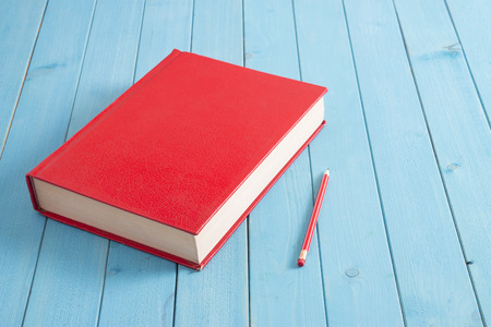 red close book and red pencil on blue tableの写真素材