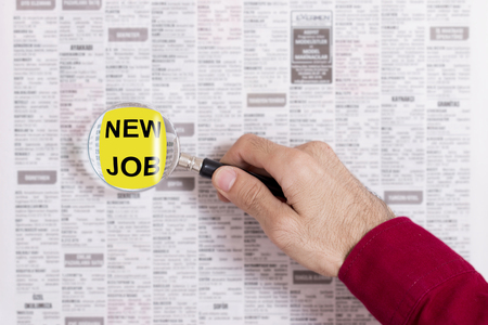 Man looks at the newspaper with the magnifying glass, to find a jobの写真素材