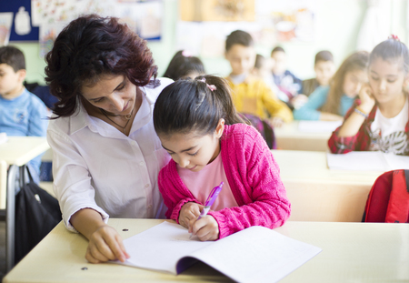 Teacher teaches to write to the girl student in the classの写真素材