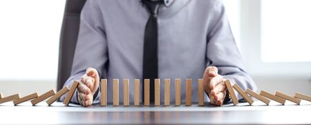 business man blocks falling blocks with his hands to prevent domino effect