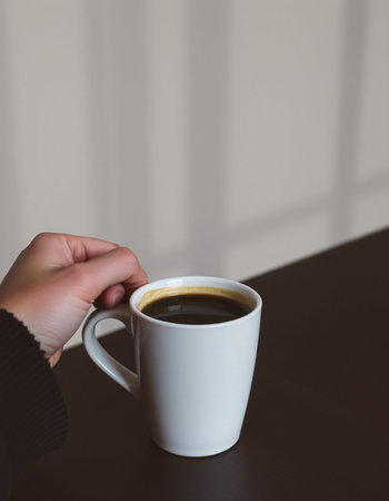 Close-up of a female hand holding a cup of black coffee