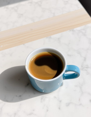 Blue cup of coffee on white marble table in morning sunlight, stock photo