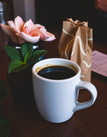 Coffee cup and flower on wooden table in coffee shop.