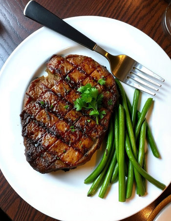 Grilled beef steak on white plate with green beans and cutlery