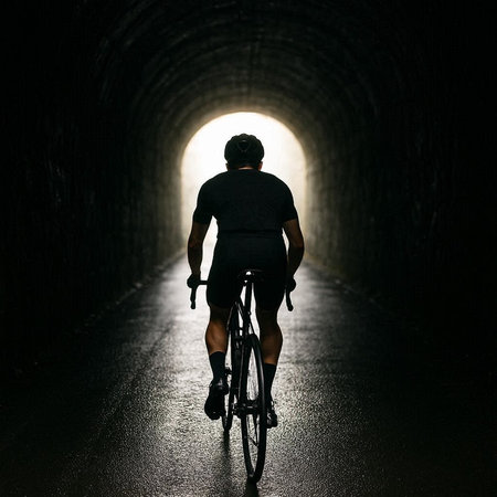 Cyclist riding bicycle in dark tunnel with light at the endの写真素材