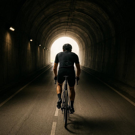 Cyclist riding a bicycle in a tunnel with light at the endの写真素材