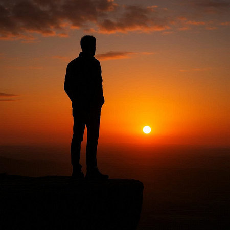 Silhouette of a man standing on top of a mountain at sunset