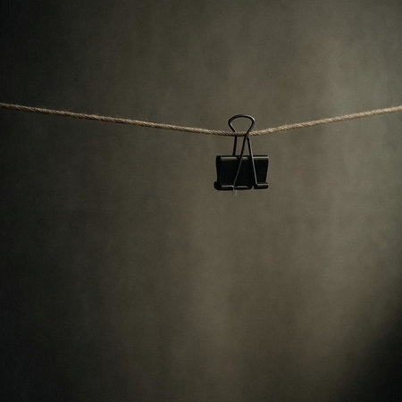Black paper clip hanging on a rope on a dark background with copy space