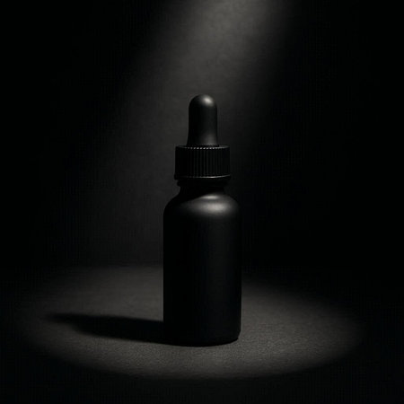 Black glass dropper bottle on dark background. Mockup for designの写真素材