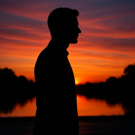 Silhouette of a man at sunset on the river bank.