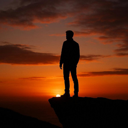 Silhouette of a man standing on the edge of a cliff at sunset