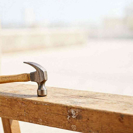 Hammer on a wooden bench in front of a blurred background.