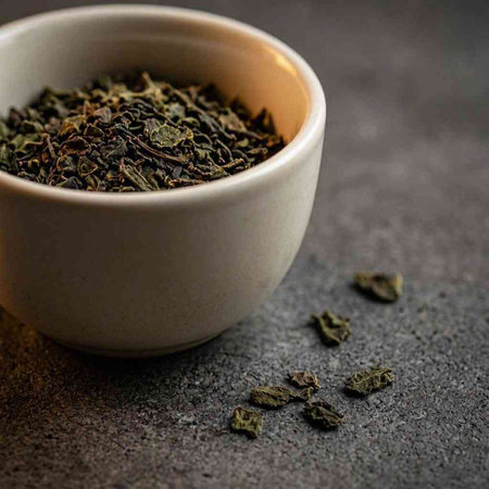 Dry green tea leaves in a white bowl on a dark background.