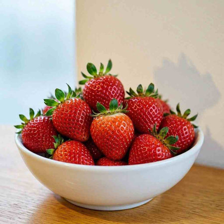Strawberries in a white bowl on a wooden table. Selective focus.