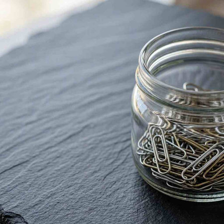 Metal paper clips in a glass jar on a black stone background.