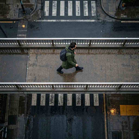 A man in a green jacket and a black cap is walking down the pedestrian crossing.