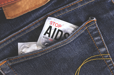 world aids day condom in jeans back pocket with wooden table background, vintage tone and over lightの写真素材
