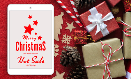 shopping concept. merry christmas tablet computer and gift box with white ribbon on red velvet background. over lightの写真素材