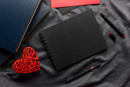 happy valentine's day concept, black book, red heart and pen on gray cloth with over light in the background. space for textの写真素材