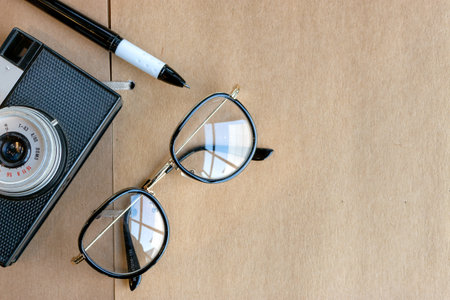 closeup old glasses, classic camera and pen on open book on table with soft-focus and over light in...
