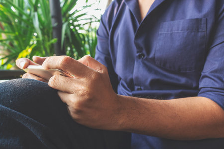 closeup of smartphones in the hands of a man sitting in a cafe shop with soft-focus and over light in the backgroundの写真素材
