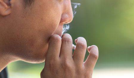 closeup young man smoking a cigarette with soft-focus and over light in the backgroundの写真素材