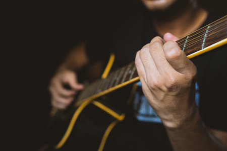 closeup man playing guitar in dark room with soft-focus and over light in the background 01の写真素材