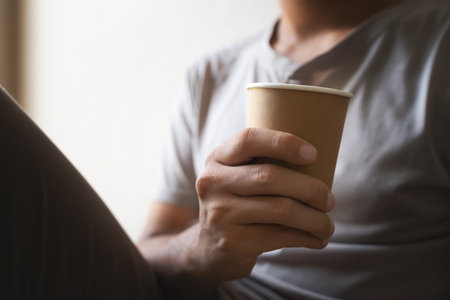 closeup hand holding paper cup of coffee in  in the room with soft-focus and over light in the...