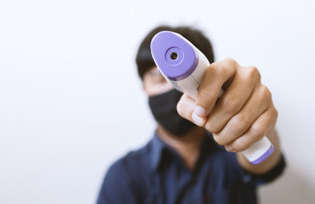 closeup hand holding infrared thermometer with soft-focus and over light in the background