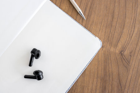 top view of blank open notebook page, pencil and wireless headphones on wood table background in...